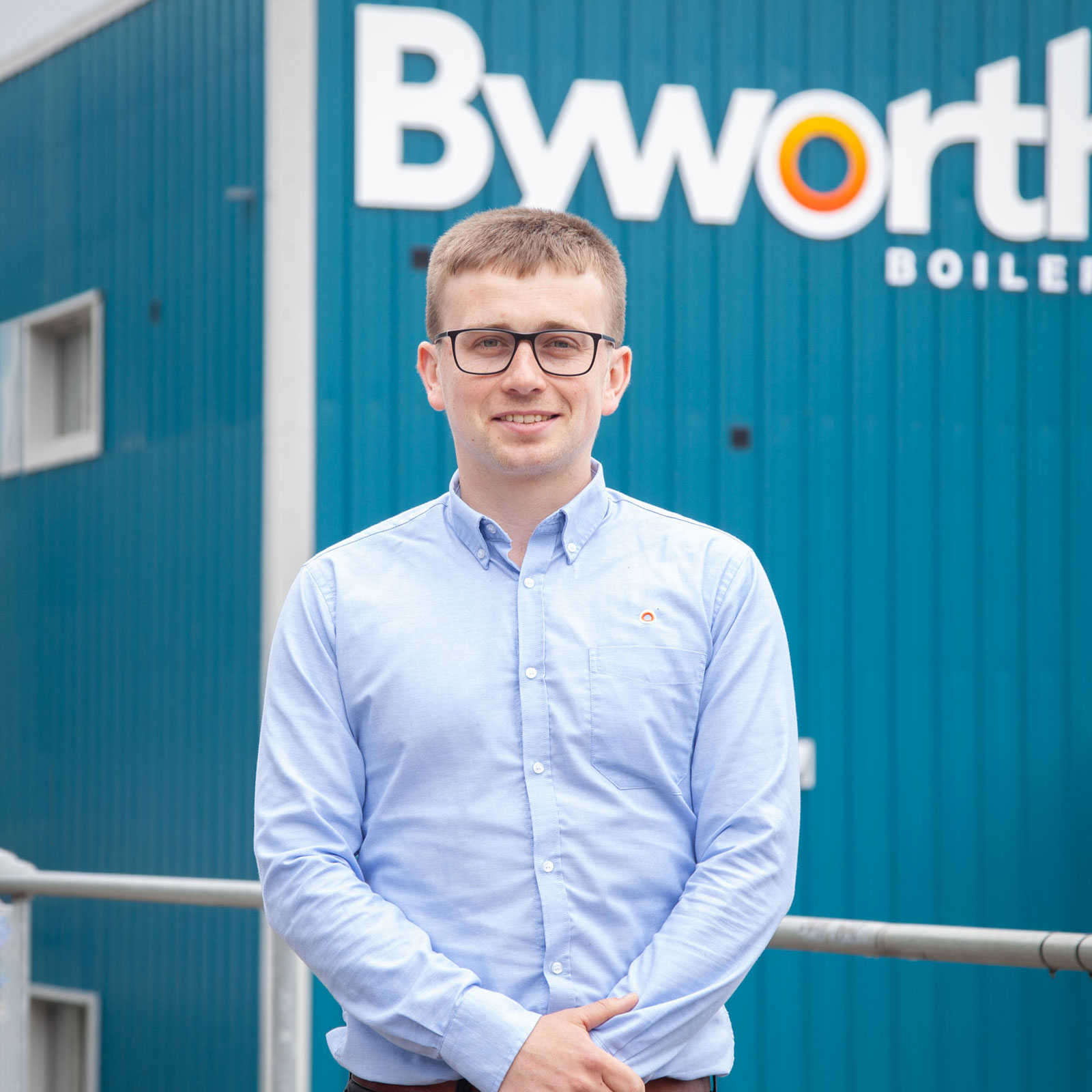 Man stood smiling with his arms folded in front of a blue building 